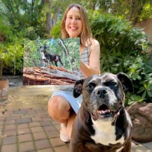 A woman kneels next to her dog while holding up a photo of her dog that was taken by Jonathan of Greenfield Pet Photography.